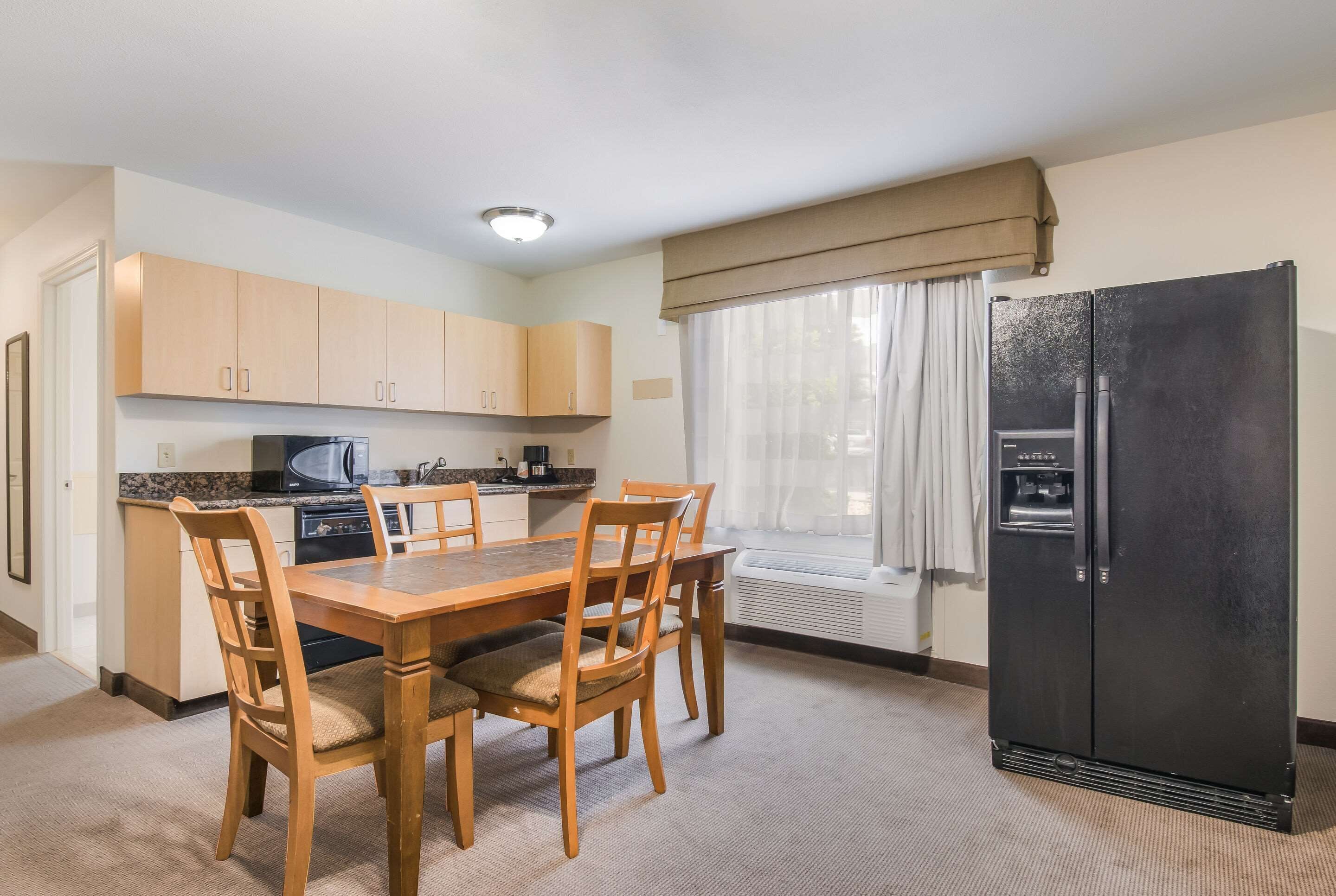 A compact kitchen with a dining table, chairs, a refrigerator, and a window with curtains.