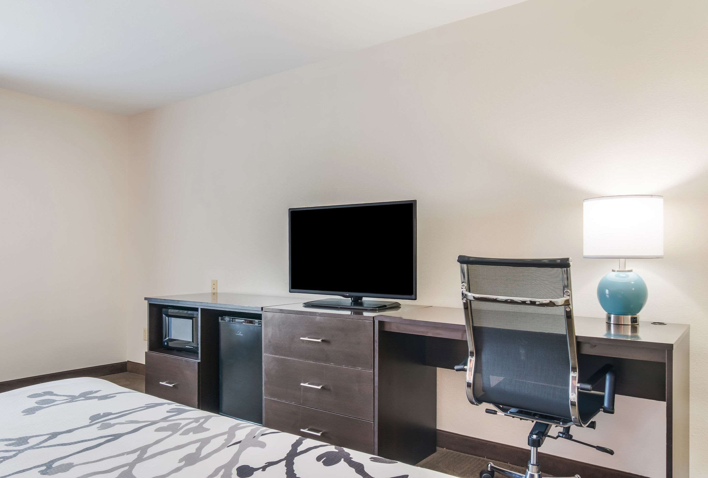 A hotel room with a bed, a desk with a television, a chair, and a lamp.