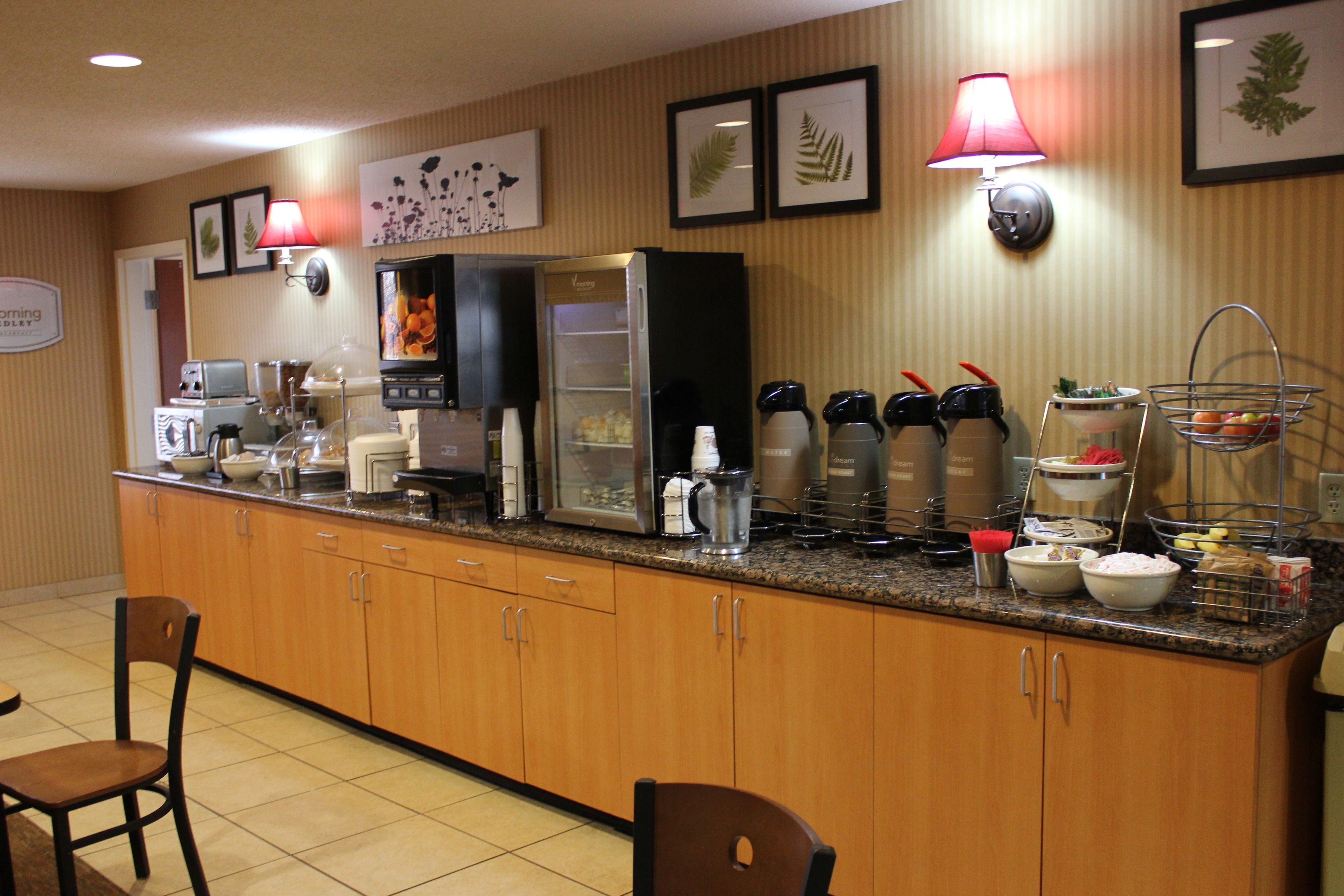 A hotel breakfast area with a self-service counter, coffee makers, and a variety of food items.