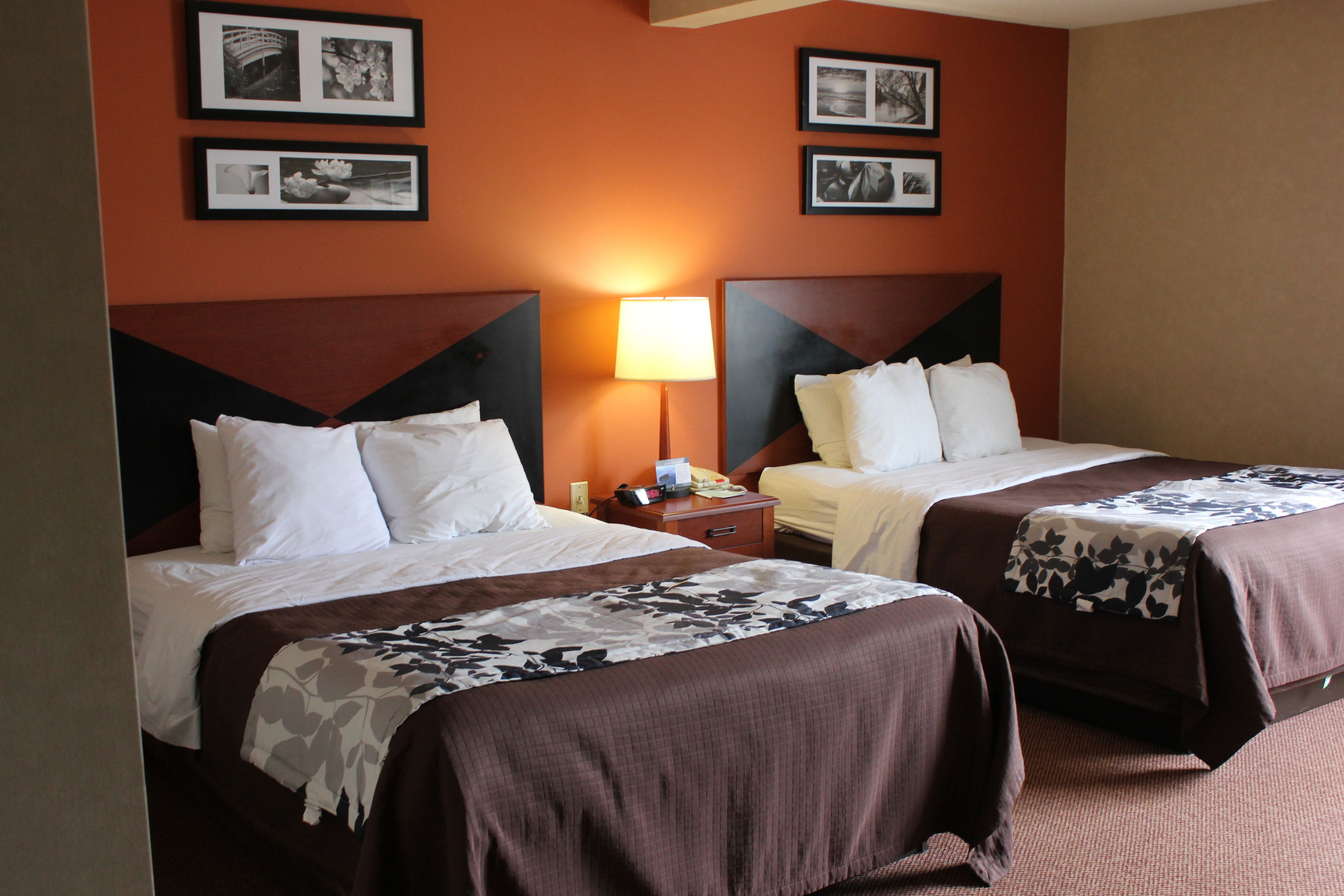 A hotel room with two beds, a nightstand, and a lamp.