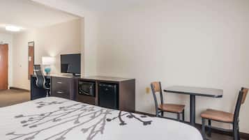 Hotelkamer met een bed, een bureau met een computer en een lamp, een magnetron, en twee stoelen.
