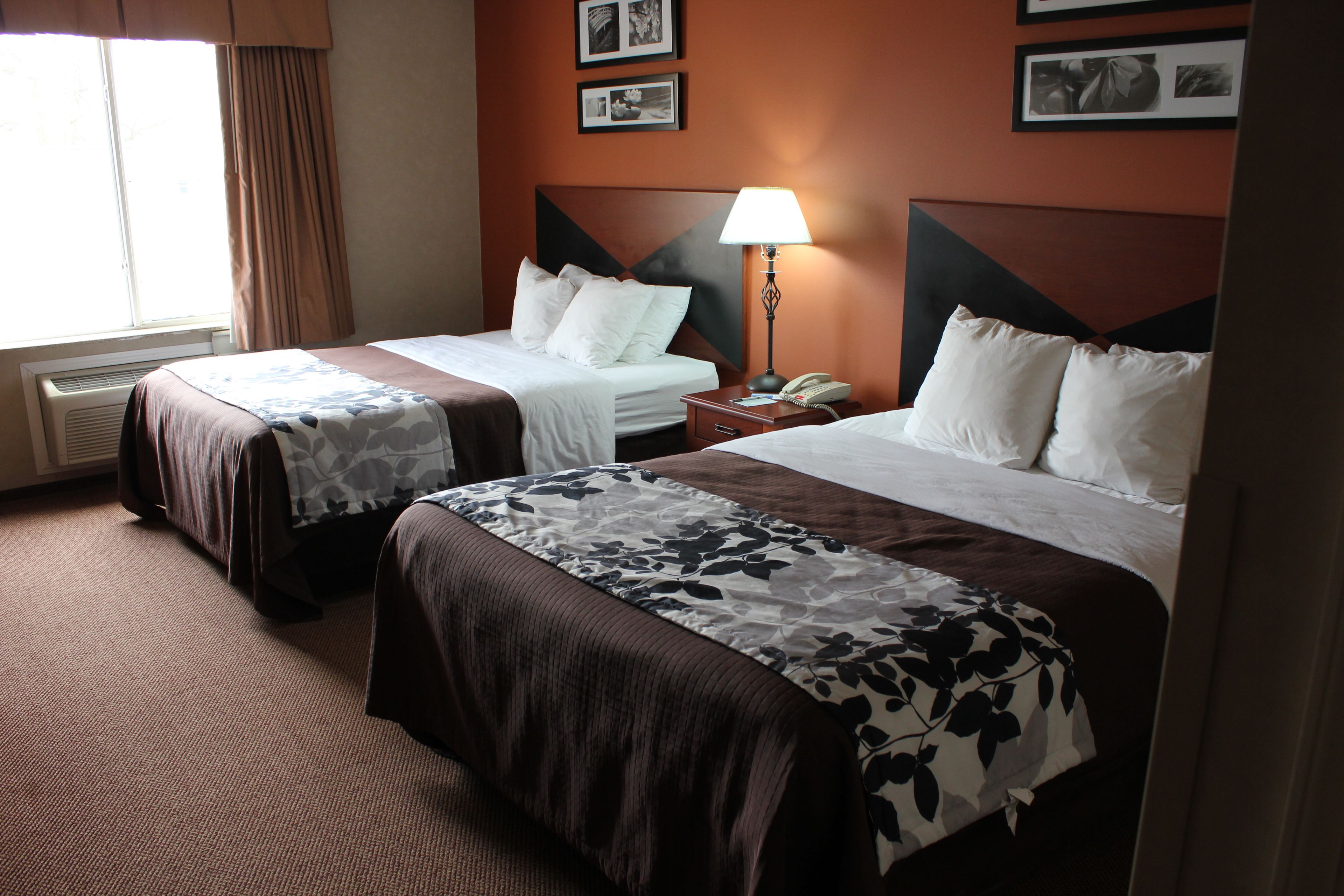 Ein Hotelzimmer mit zwei Betten, einem Nachttisch mit Lampe und gerahmten Bildern an der Wand.
