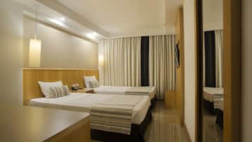 A hotel room with two beds, a wooden headboard, a bedside table, a lamp, and a large mirror.