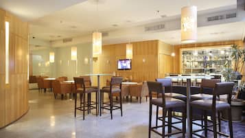 Un restaurante moderno con mesas y sillas altas, una zona de bar y una pantalla de televisión.