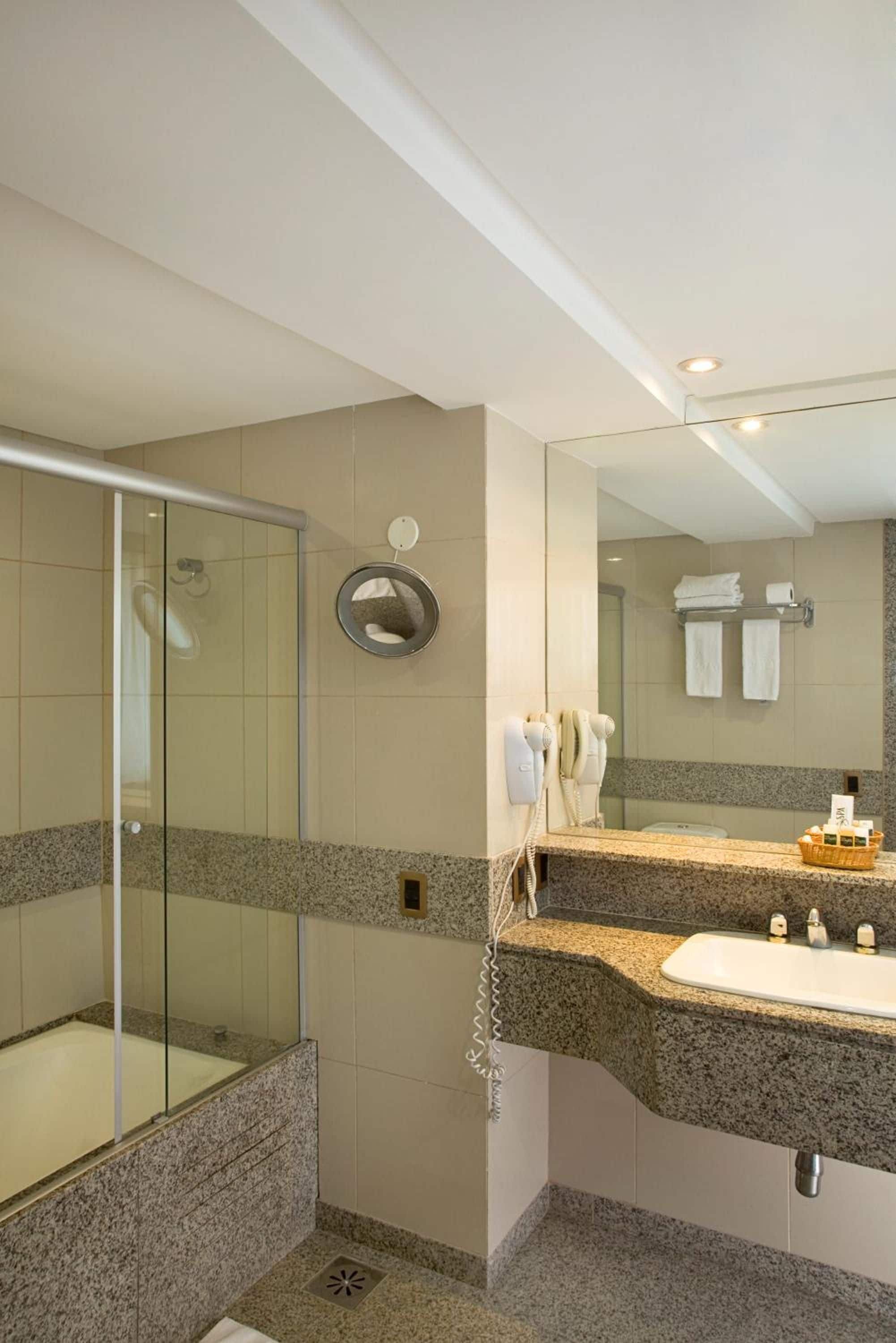 A modern bathroom with a glass shower enclosure, a granite countertop sink, and a large mirror.