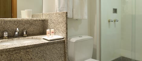 A modern bathroom with a granite countertop, a toilet, a glass shower enclosure, and a large mirror.