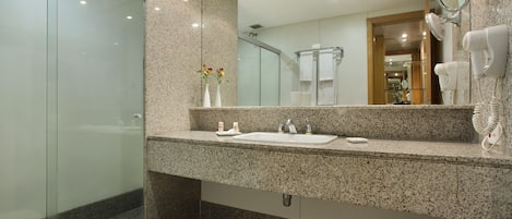 Un baño moderno con encimera de granito, cabina de ducha de vidrio, un espejo grande y un secador de pelo montado en la pared.