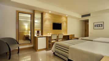 Habitación de hotel con cama, escritorio, silla, refrigerador pequeño y televisor montado en la pared.