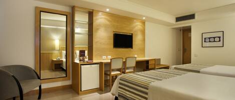 A hotel room with a bed, a desk, a chair, a small refrigerator, and a television mounted on the wall.