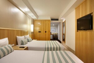Ein Hotelzimmer mit zwei Betten, einem Fernseher, einem Schreibtisch und einem Spiegel.