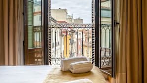 A hotel room with a bed, two towels, and an open balcony with a view of buildings. - Hotel Victoria 4 (Madrid)