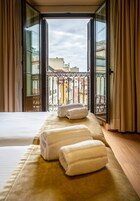 A hotel room with a bed, two towels, and an open balcony with a view of buildings.