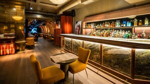 A bar area with a long counter, multiple liquor bottles, and two yellow chairs. - Hotel Victoria 4 (Madrid)