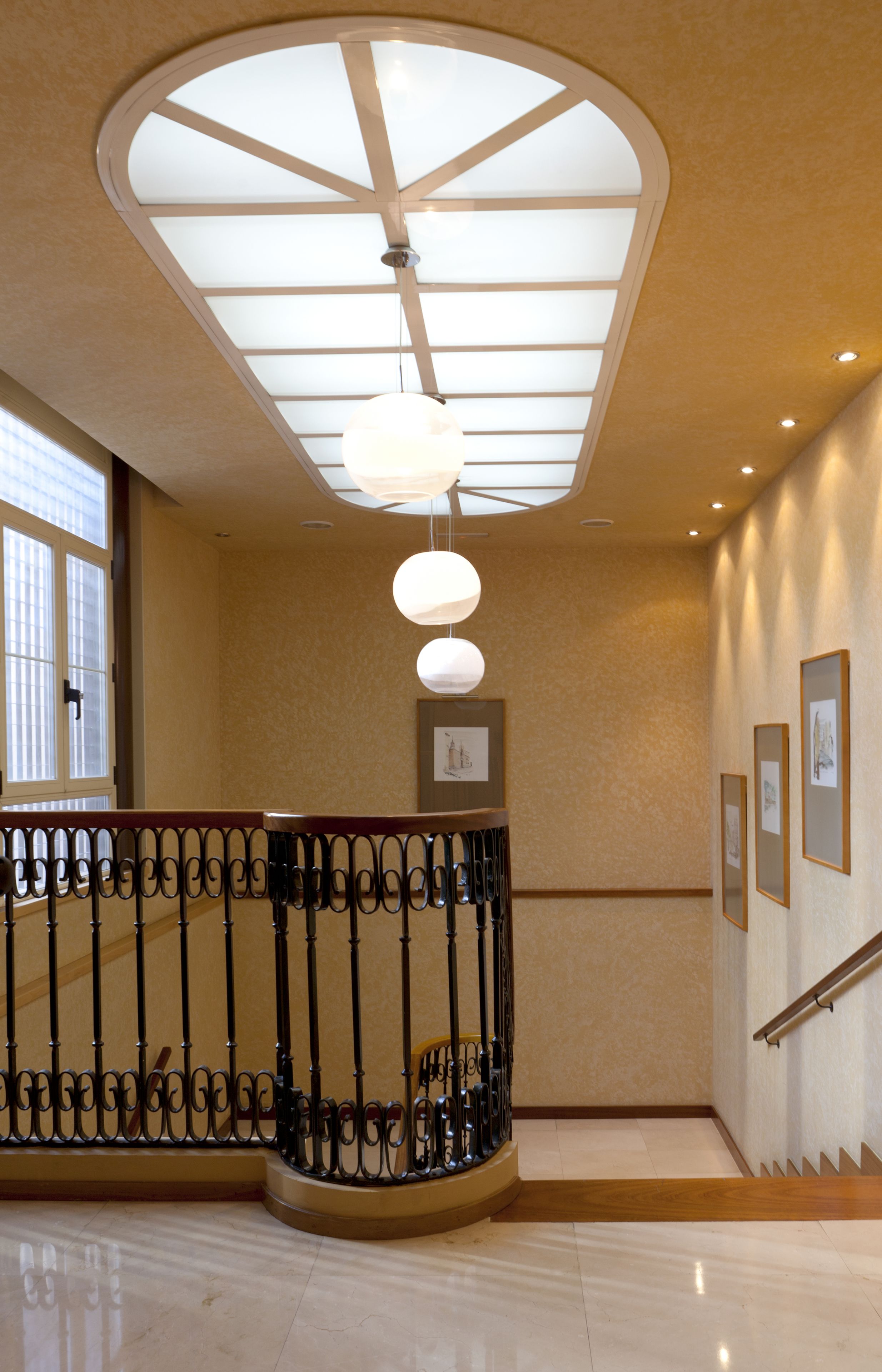 A hotel lobby with a modern design, featuring a glass ceiling, a curved railing, and framed artwork on the walls.