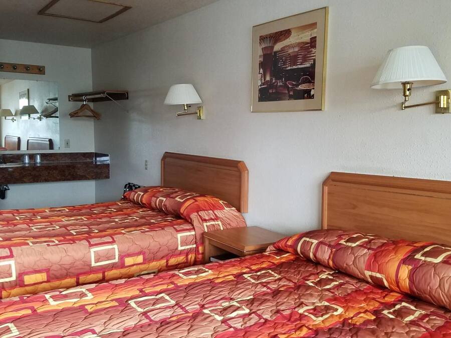 Ett hotellrum med två sängar, en sänggavel i trä, en spegel, ett litet bord och två vägglampor.