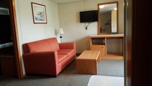 A compact room with a red sofa, a wooden desk, a television, and a mirror.