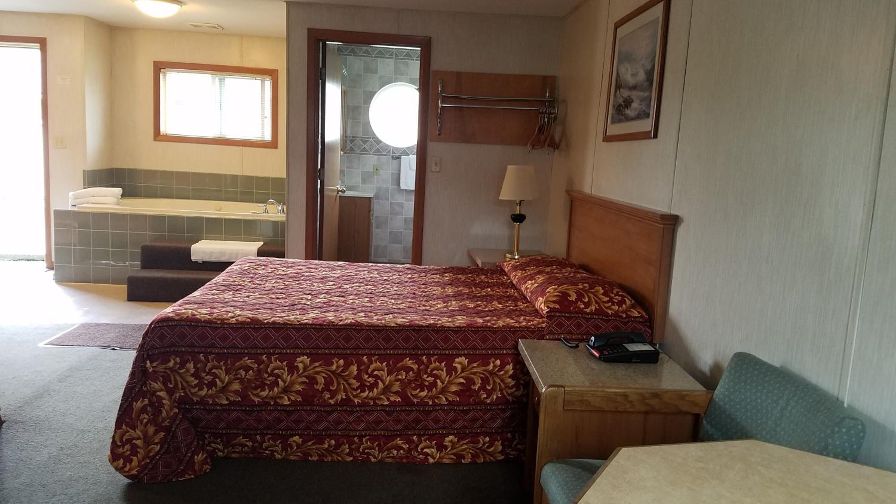 Ein Hotelzimmer mit Bett, kleinem Tisch, Stuhl, Schreibtisch, Lampe und einem Badezimmer mit Badewanne sowie einem Fenster.