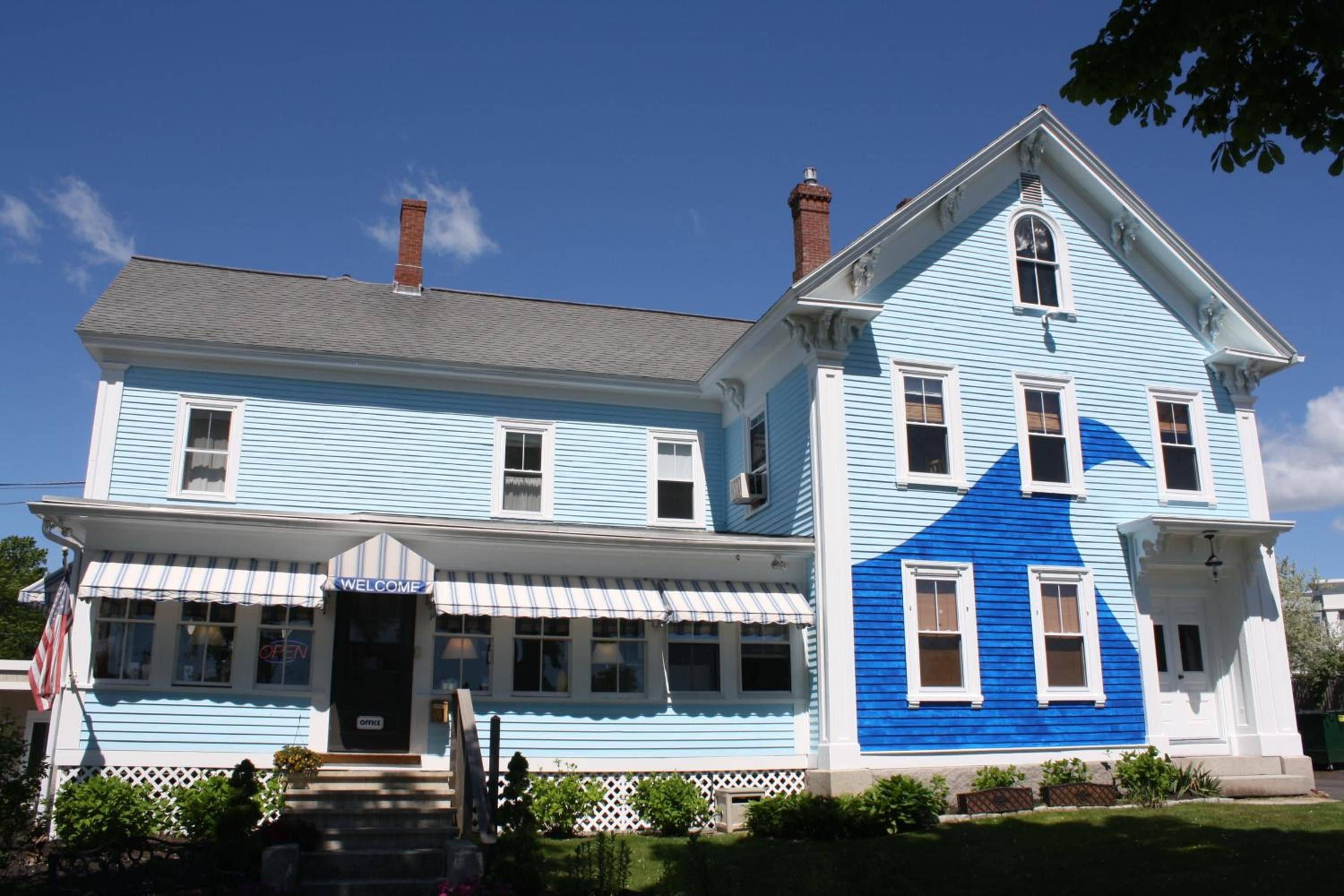 Un bâtiment à deux étages aux couleurs bleu et blanc, avec une entrée principale agrémentée d’une pancarte « BIENVENUE » et une pancarte « OUVERT » bien visible sur la porte.