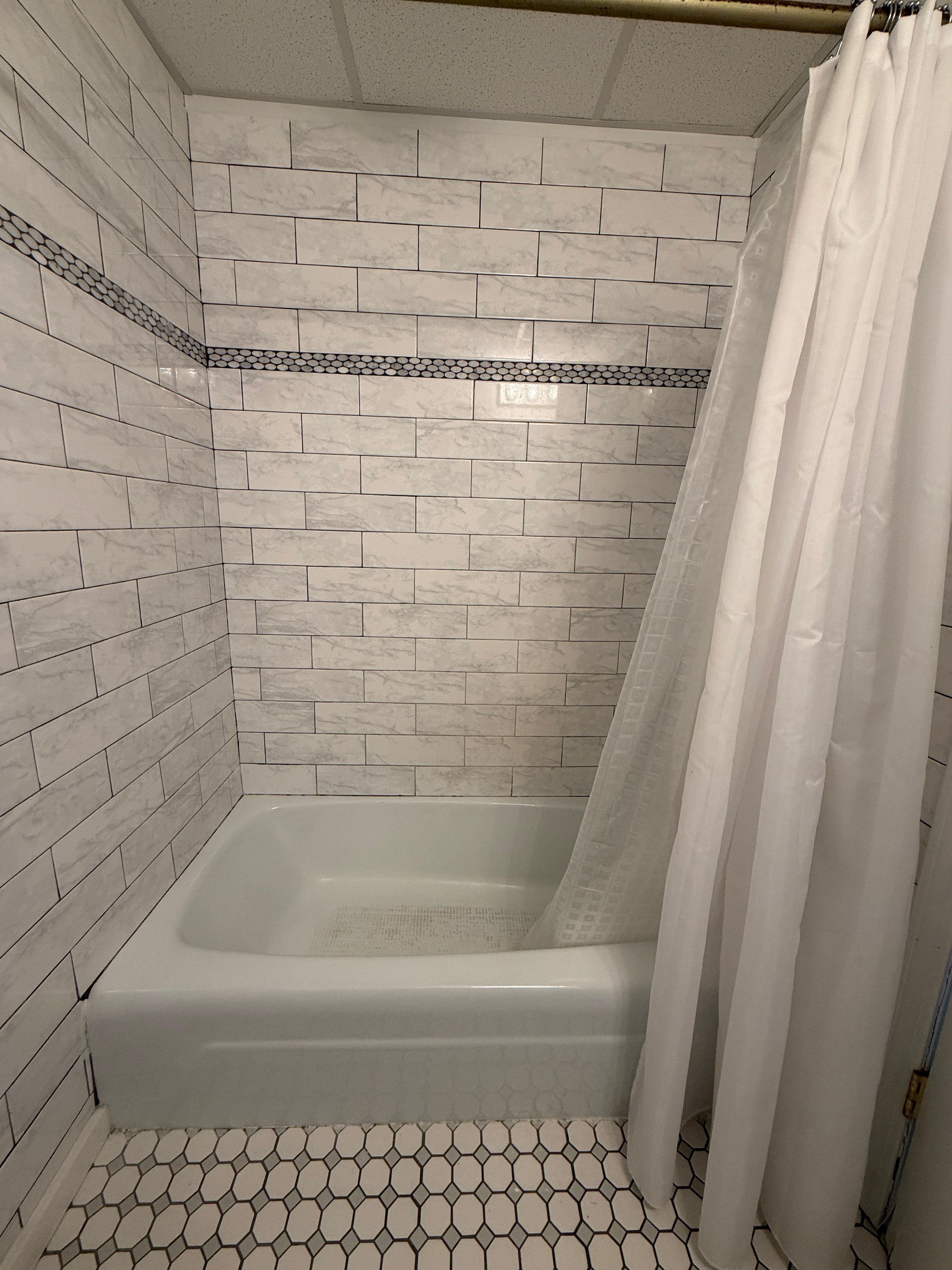 A shower area with white marble tiles, a white bathtub, and a shower curtain.