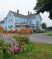 A large two-story building with a porch, surrounded by a well-maintained lawn and flowering plants.