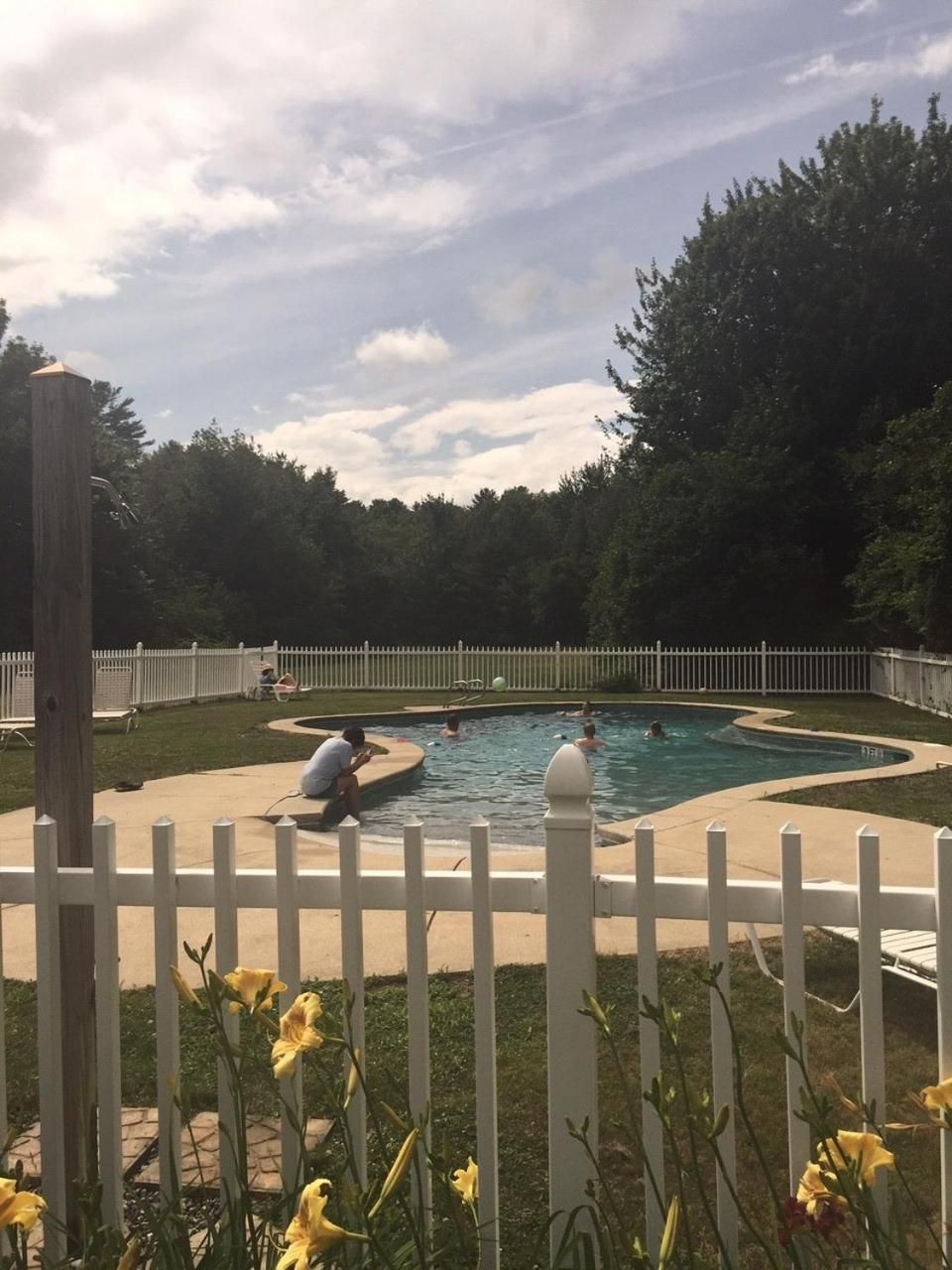 Una piscina con una cerca blanca, rodeada de árboles y un cielo nublado.