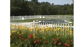 Un jardín con cerca blanca, un estanque circular y diversas flores.