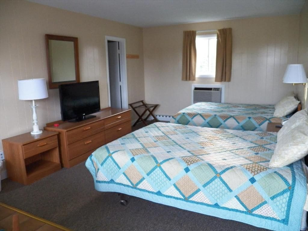 Une chambre d’hôtel avec deux lits, un bureau avec une télévision, une chaise et un appareil de climatisation.