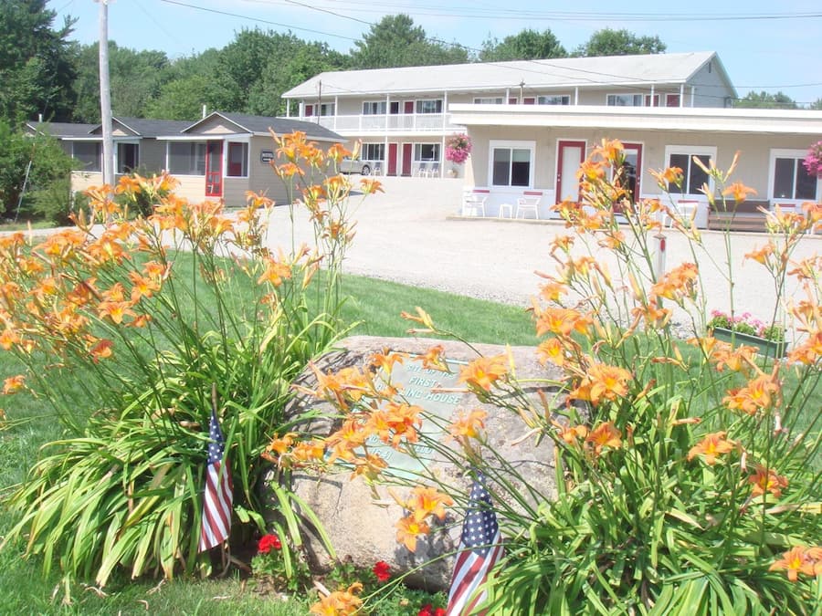 A motel with a front lawn, a large rock with an American flag, and a sign reading "Motel First".
