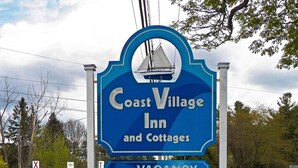 Letrero del Coast Village Inn and Cottages anunciando habitaciones disponibles, suites Queens Kings y comodidades como una piscina excelente.