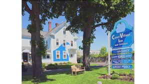 Un edificio grande y blanco con techo azul, rodeado de árboles y un cartel anunciando un hotel con habitaciones disponibles.