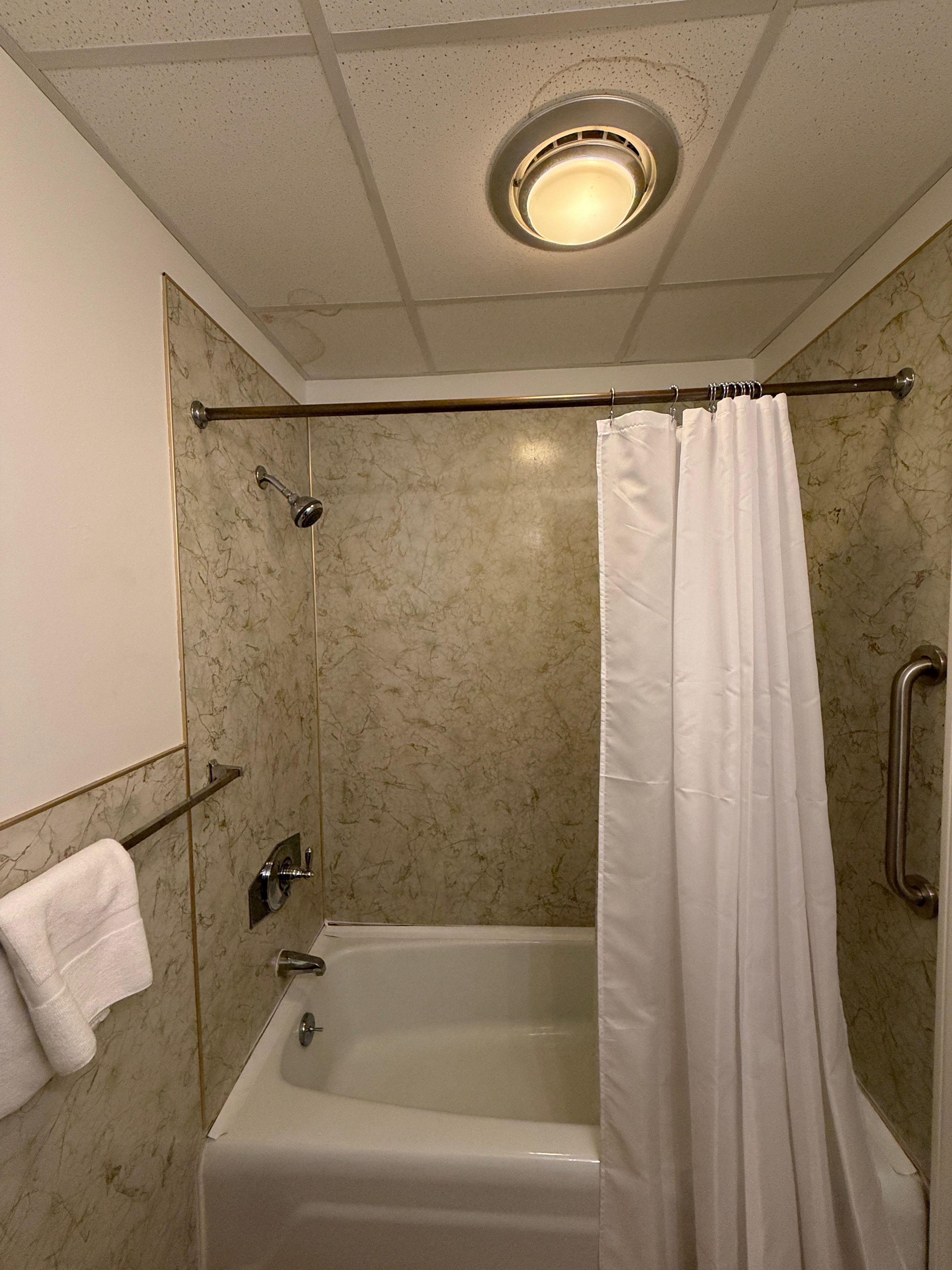 A bathroom with a bathtub, a shower curtain, a towel rack, and a ceiling light.