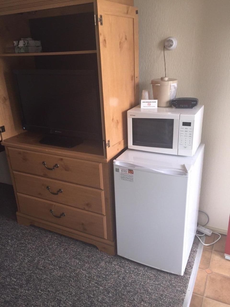 A compact kitchenette with a microwave, a small refrigerator, and a wooden cabinet with a television.