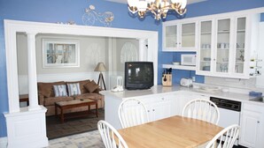 Una cocina compacta con armarios blancos, una mesa de comedor de madera y un televisor.