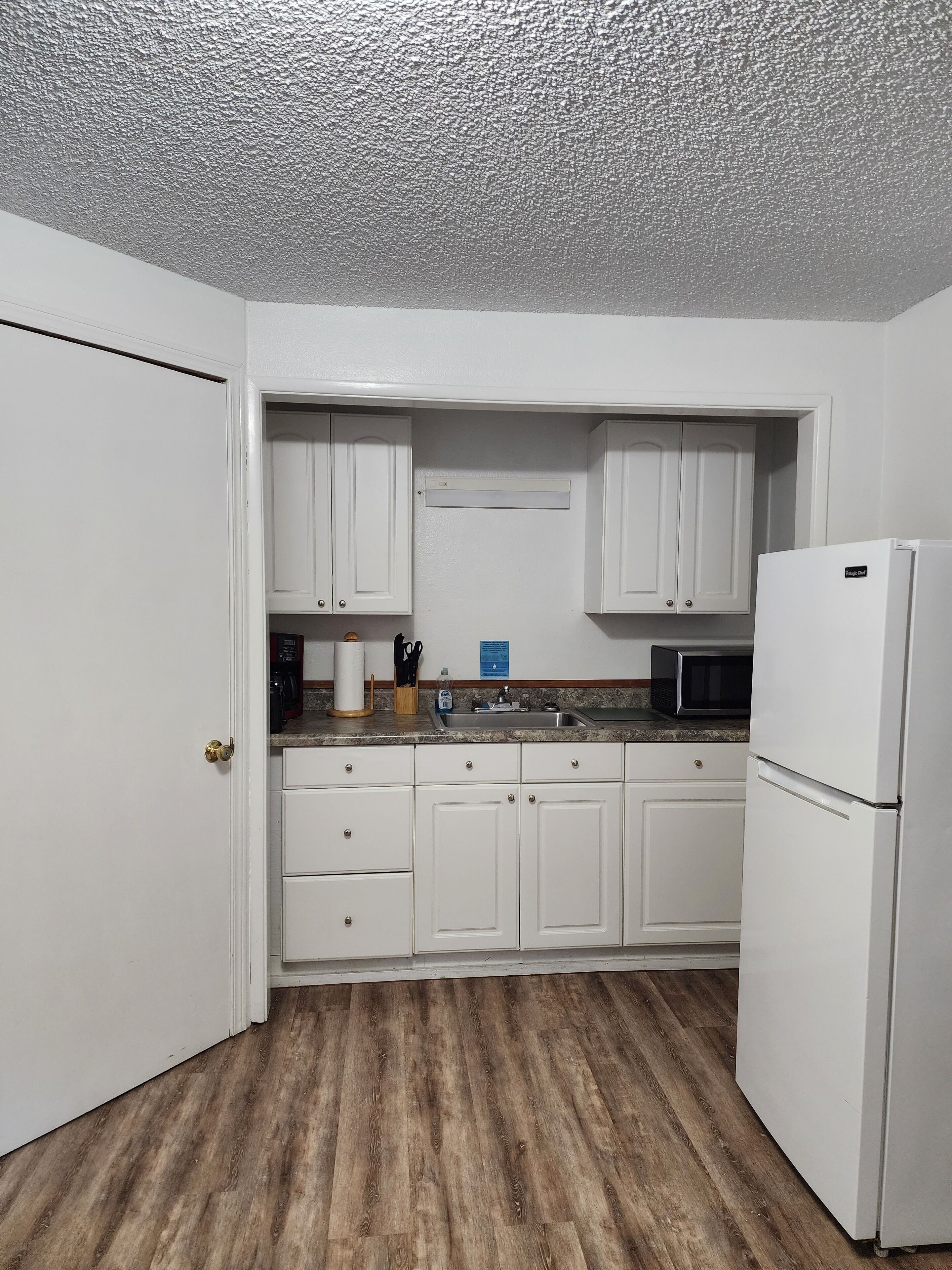 A kitchen with white cabinets, a stainless steel sink, a microwave, and a refrigerator.