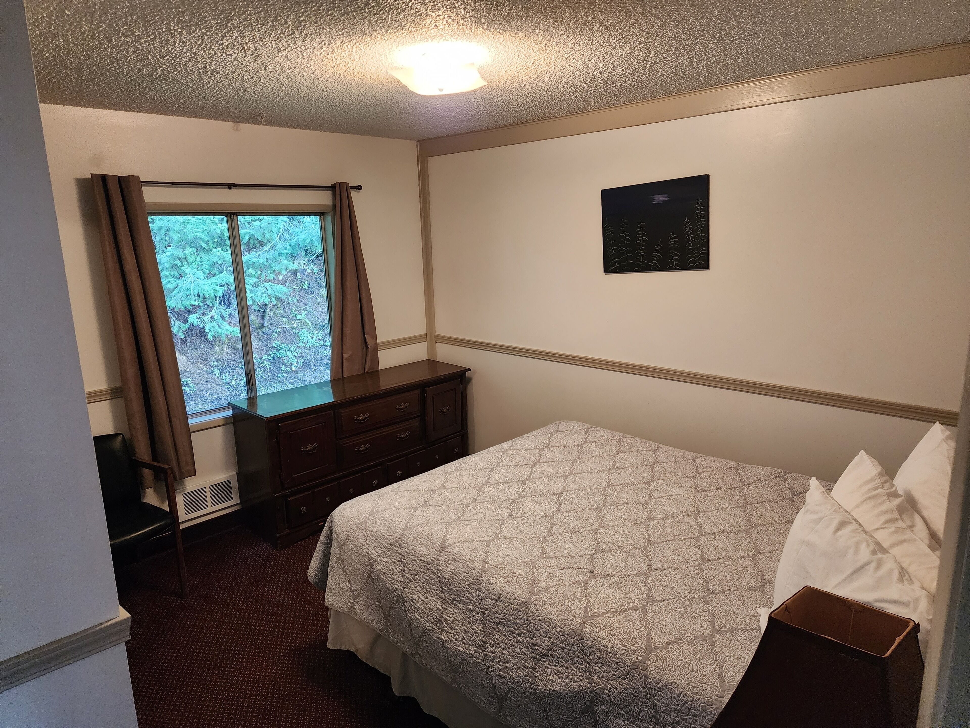 A bedroom with a bed, a dresser, a window with curtains, and a wall-mounted artwork.