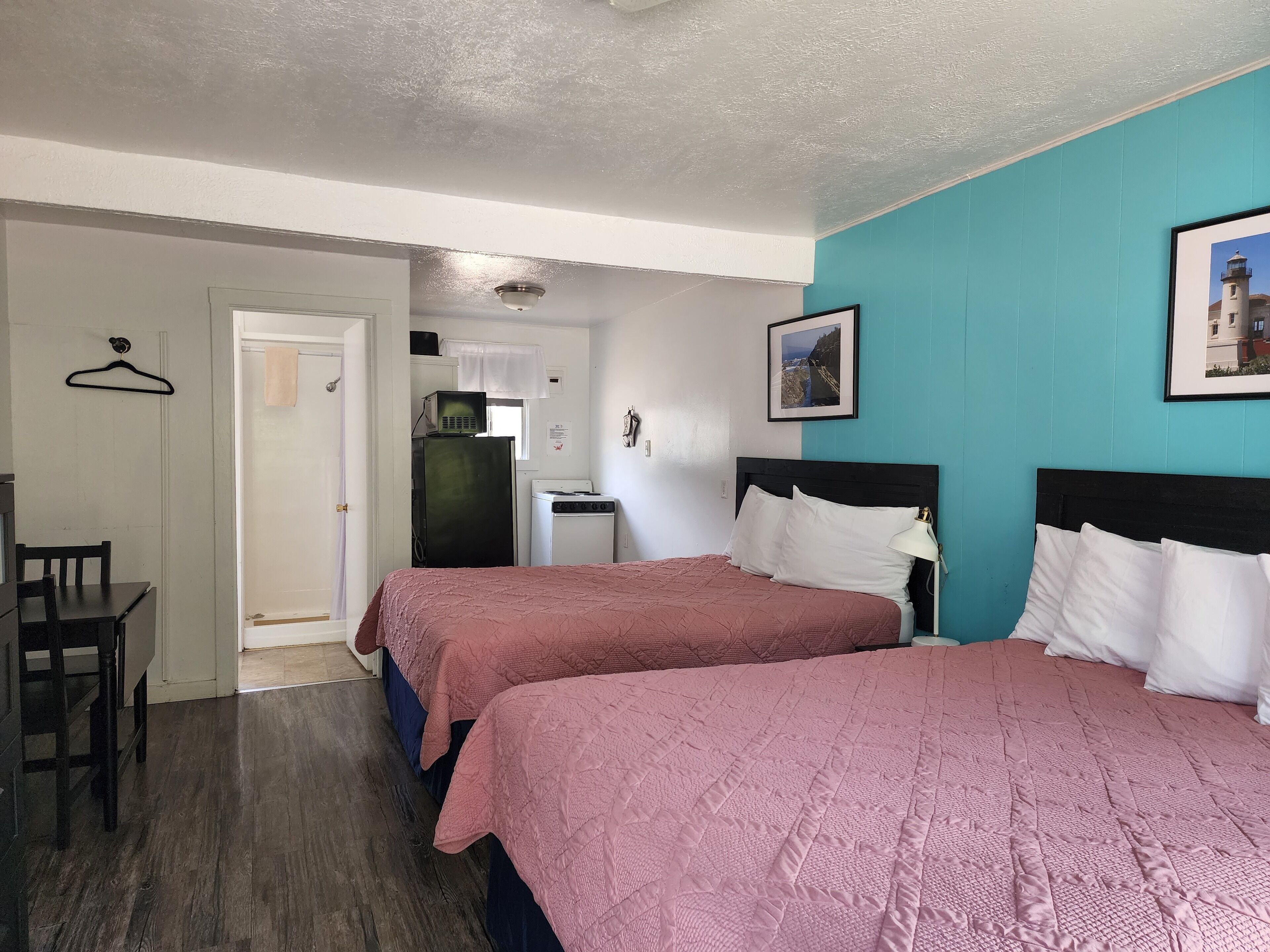 A hotel room with two beds, a desk, a chair, a kitchenette, and a bathroom.