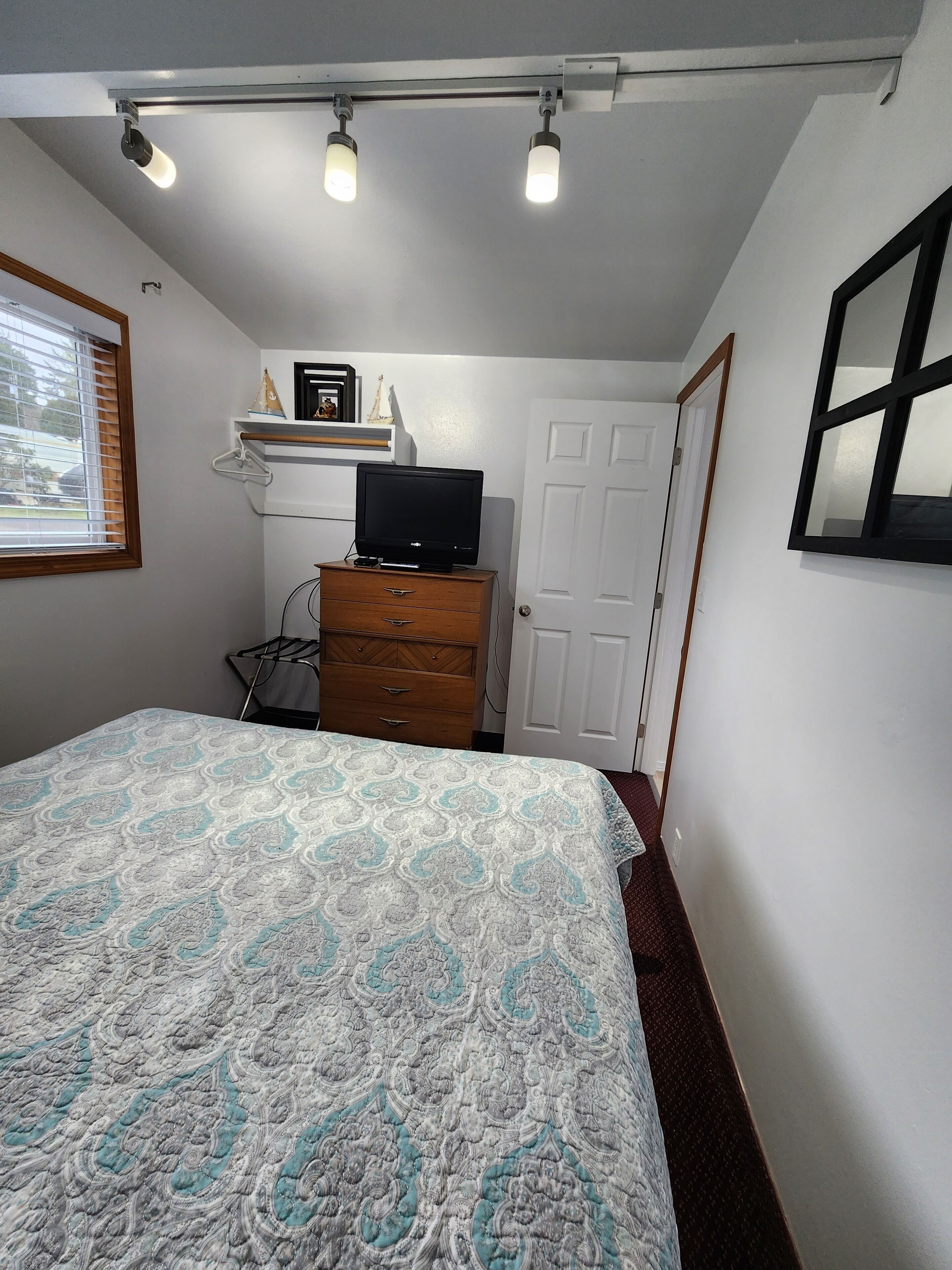 A bedroom with a bed, a dresser, a television on a shelf, and a door.