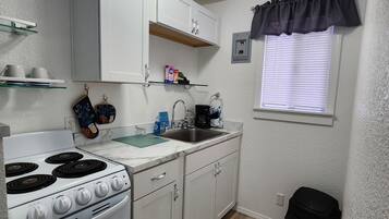 A compact kitchen with white cabinets, a white stove, and a black trash bin.