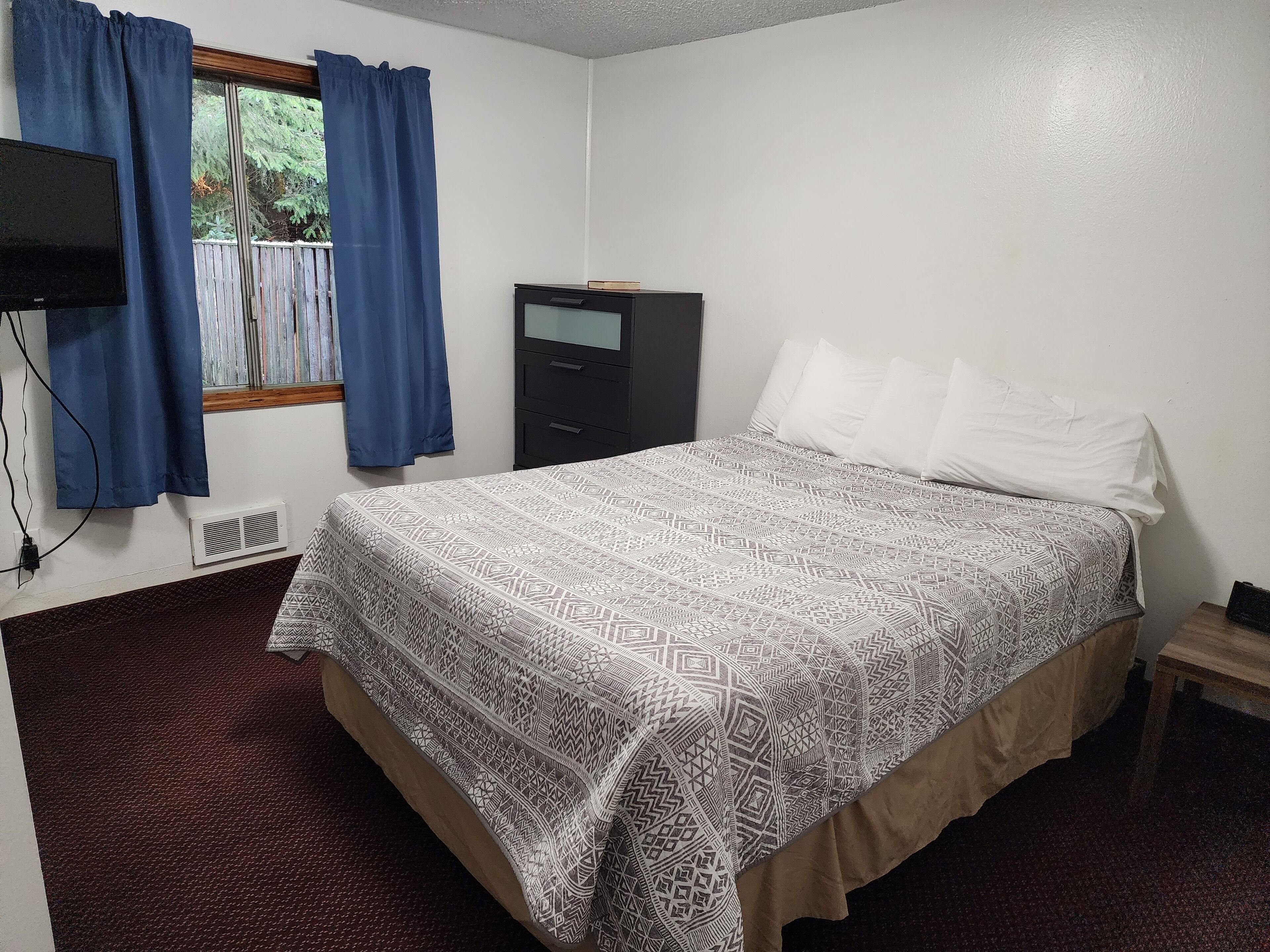 A bedroom with a bed, a dresser, a TV, and a window with curtains.