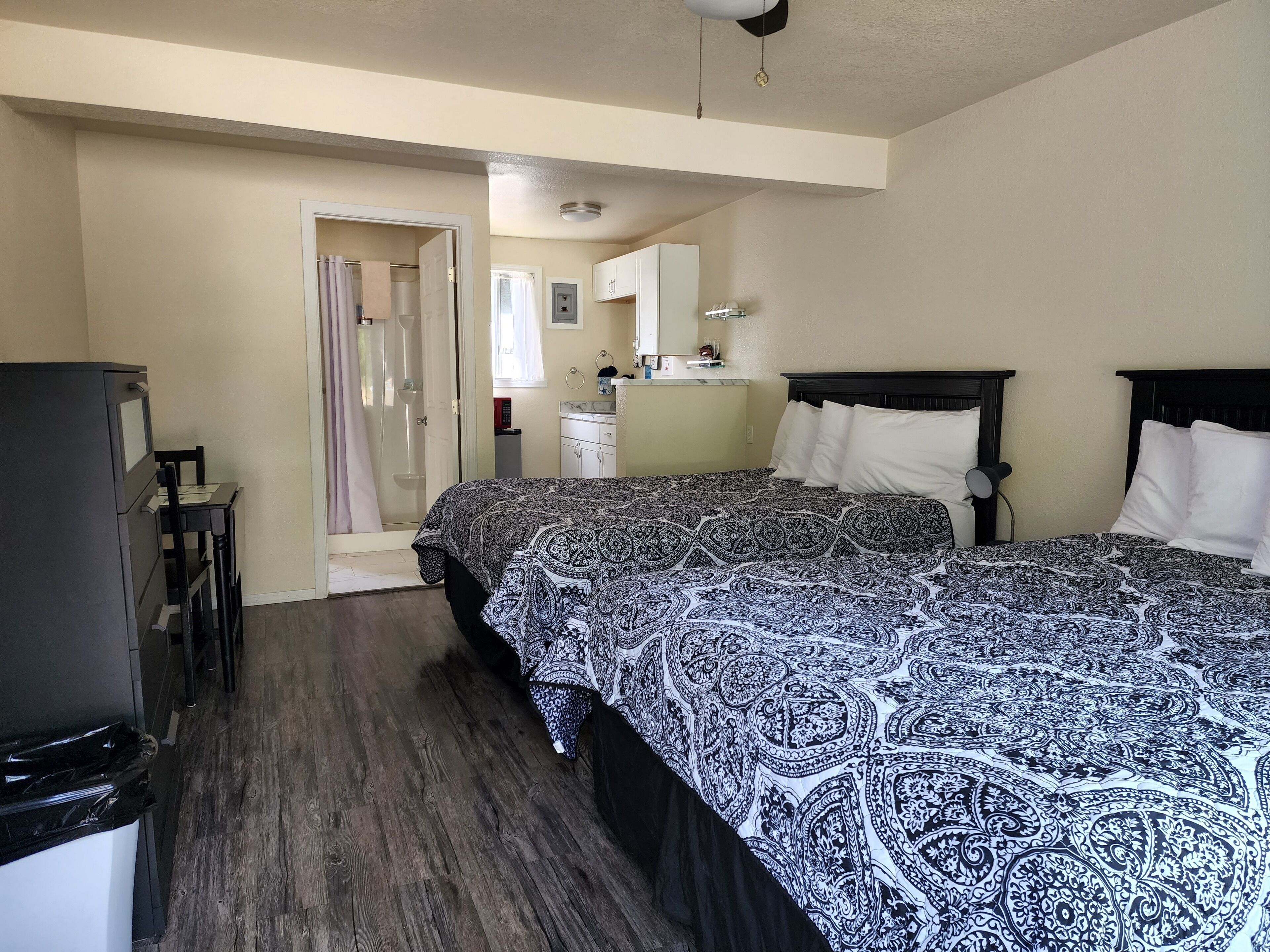 A bedroom with two beds, a small kitchenette, and a bathroom with a shower.