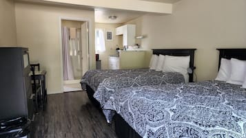 A bedroom with two beds, a small kitchenette, and a bathroom with a shower.