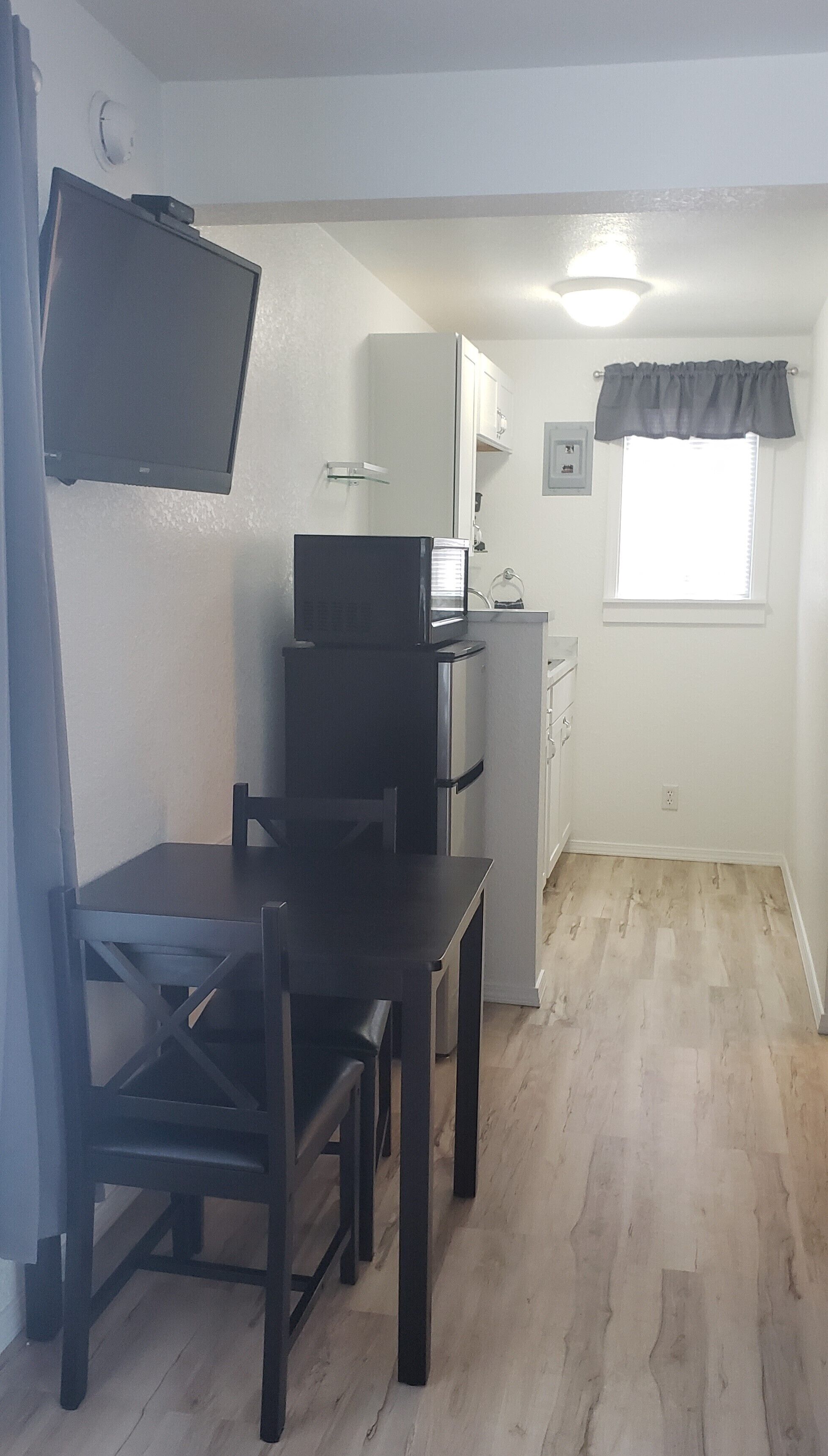 A compact kitchen with a refrigerator, microwave, and a small window with curtains.