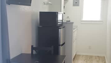 A compact kitchen with a refrigerator, microwave, and a small window with curtains.