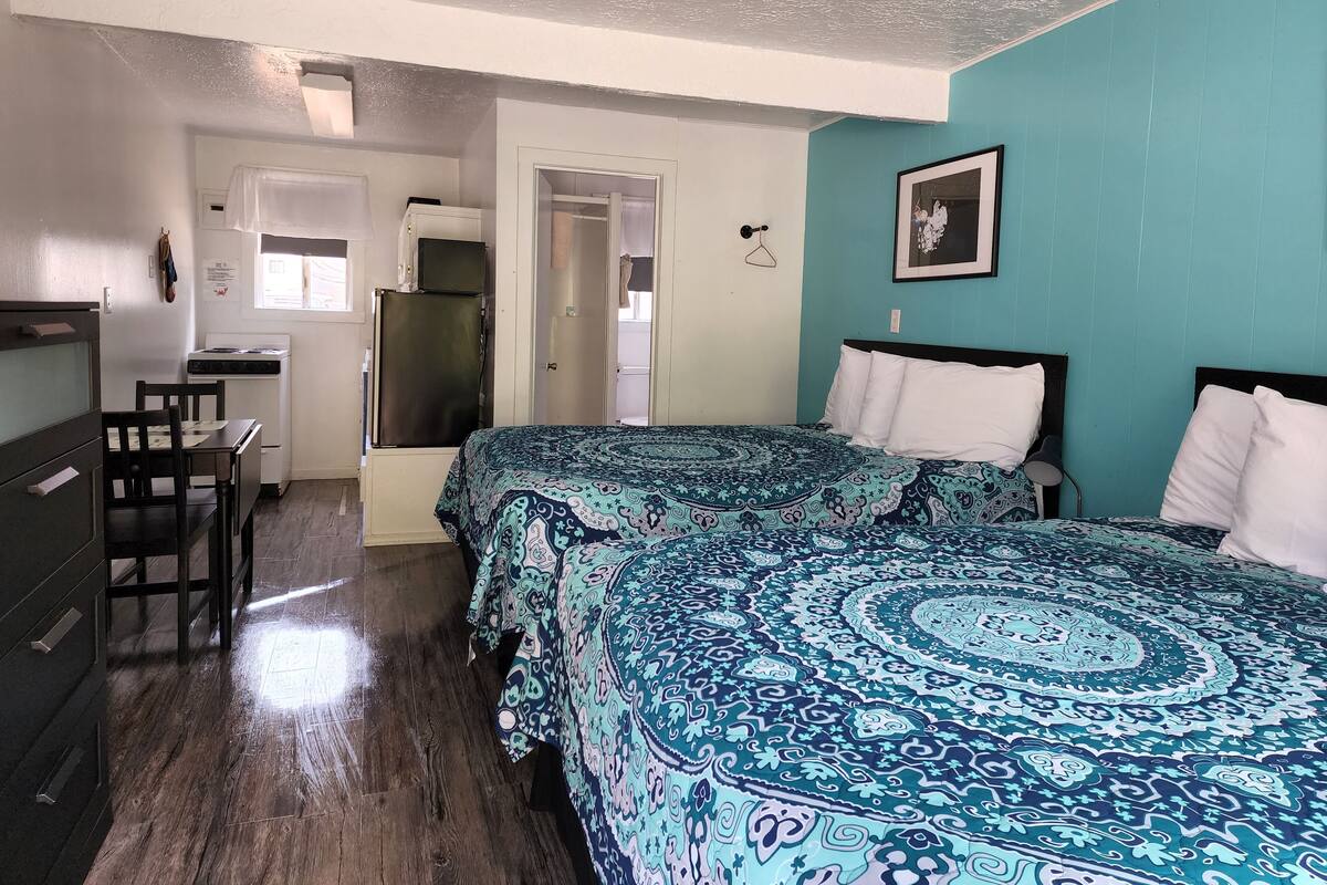 A compact bedroom with two beds, a kitchenette, and a small dining area.