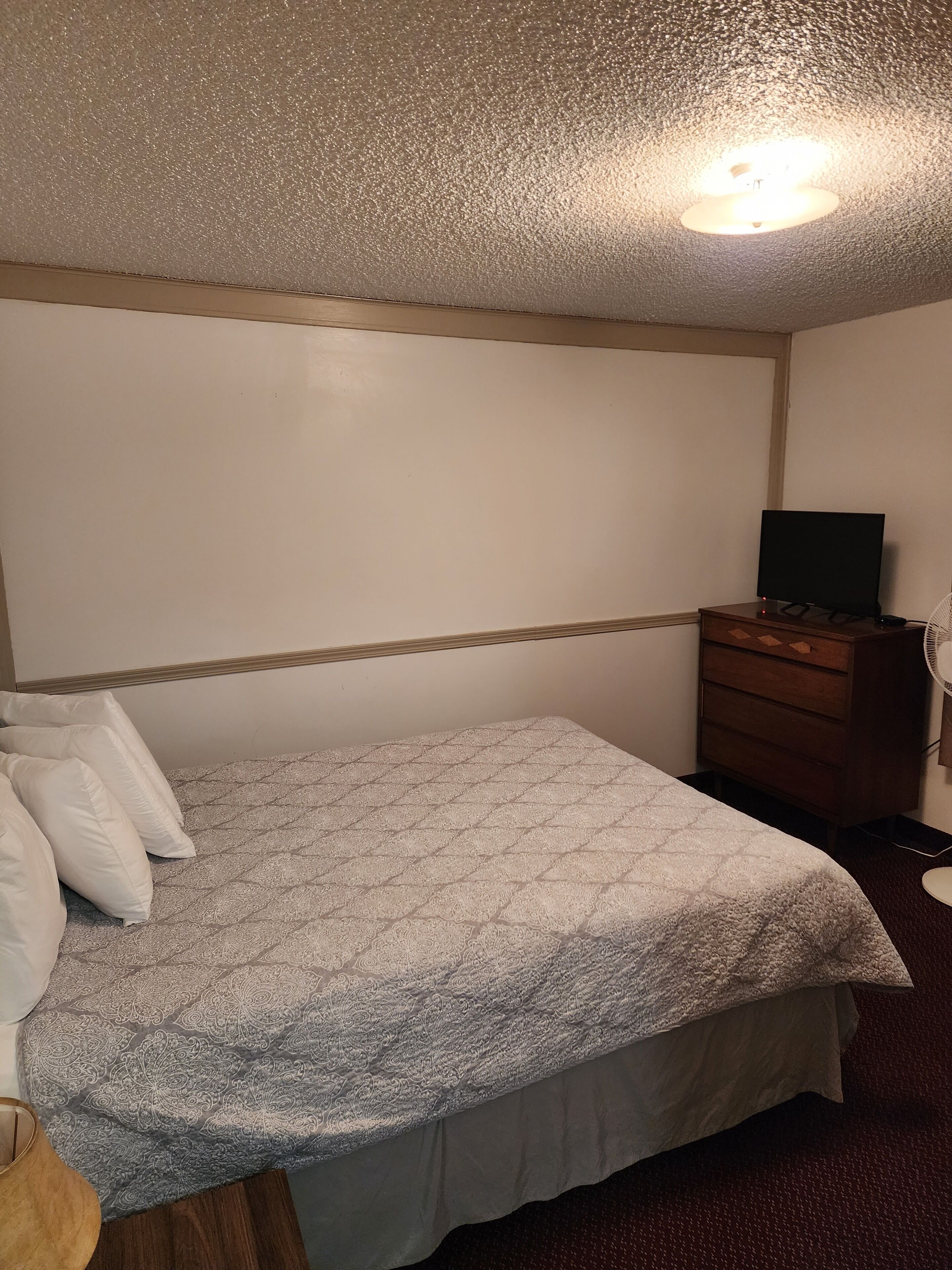 Ein Schlafzimmer mit Bett, Kommode, Fernseher und Deckenleuchte.