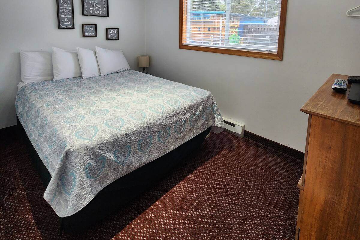 A bedroom with a bed, a window, and a desk with a telephone.