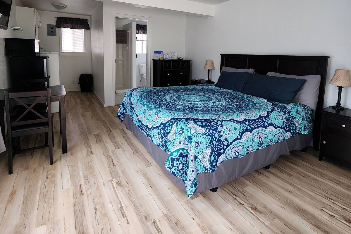A bedroom with a bed, a desk, a chair, a ceiling fan, and a window with blinds.