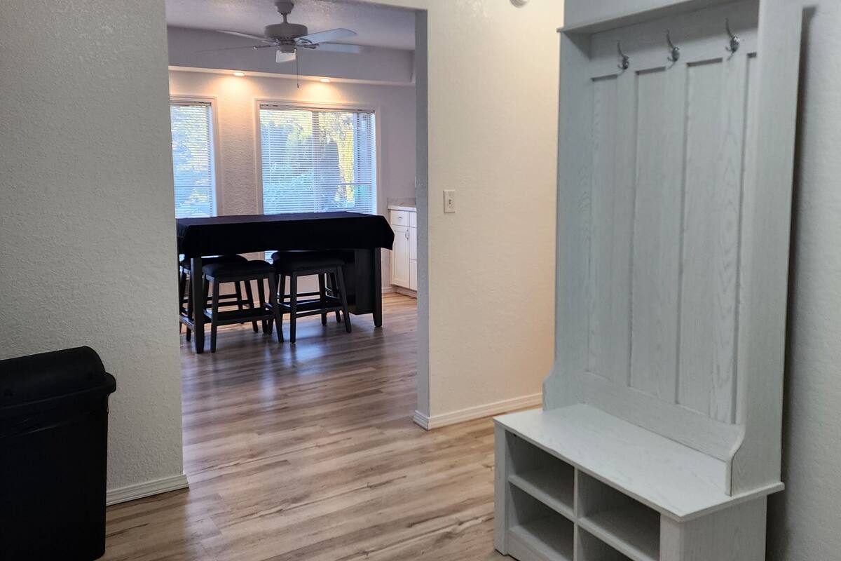 A room with a wooden floor, a dining table with chairs, a white bench, and a ceiling fan.