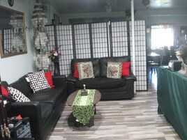 Uma sala de estar com um sofá preto, uma mesa pequena e um painel decorativo.