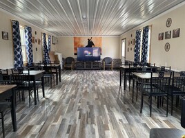 Um quarto amplo com uma mesa comprida no centro, rodeada por cadeiras, e uma tela grande exibindo o logotipo do Discovery+.